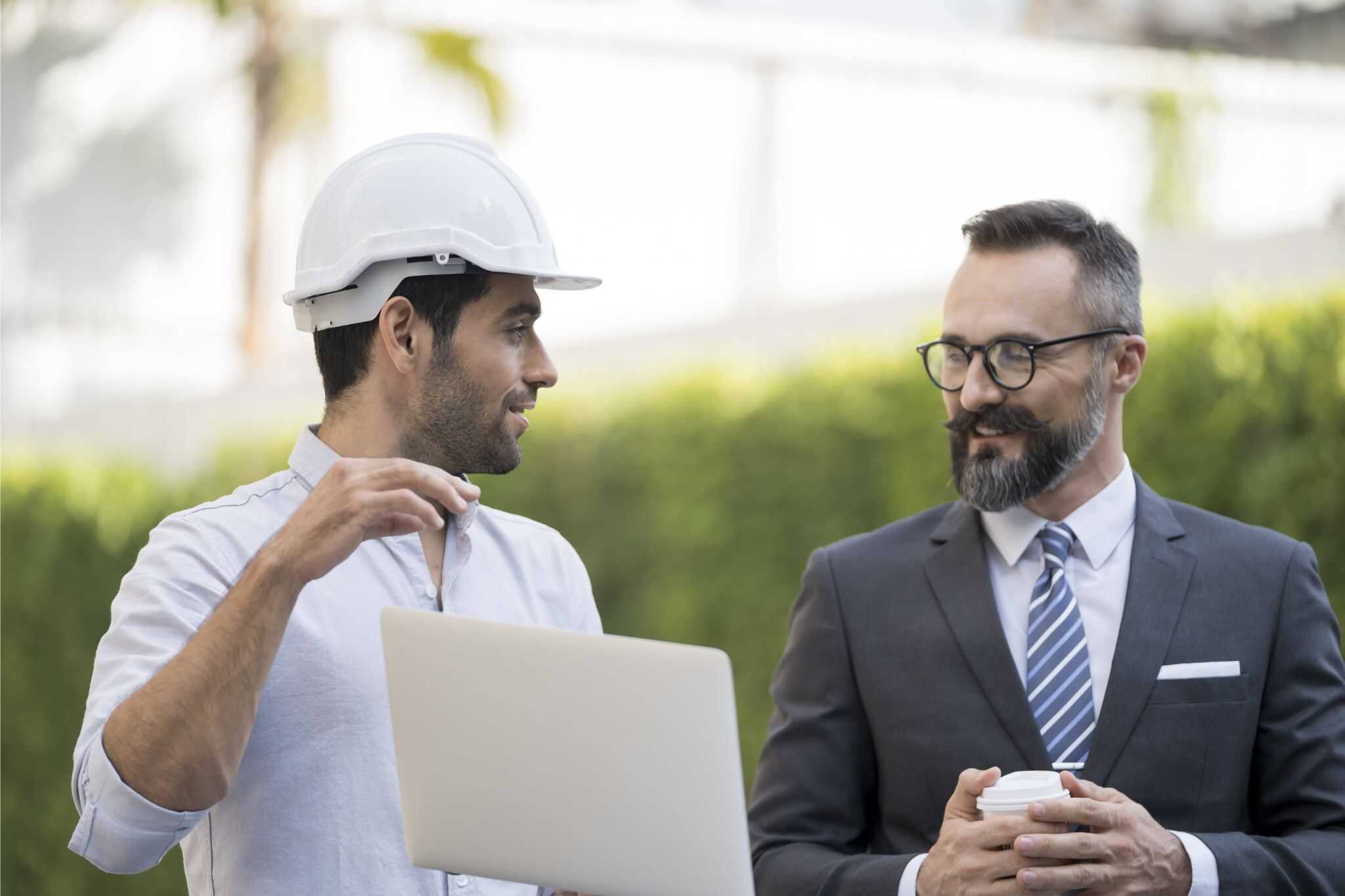 Two professionals with laptop and coffee discussing outdoors, representing industrial executive search expertise in a natural setting.