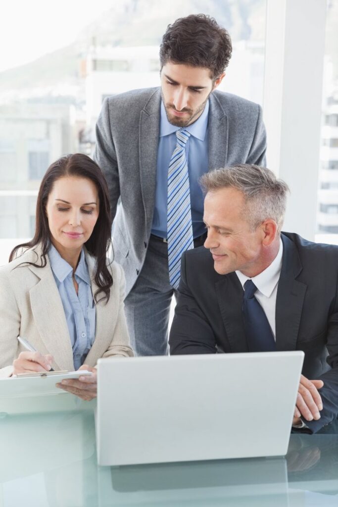 Three business professionals reviewing documents and laptop data at an executive search firm.