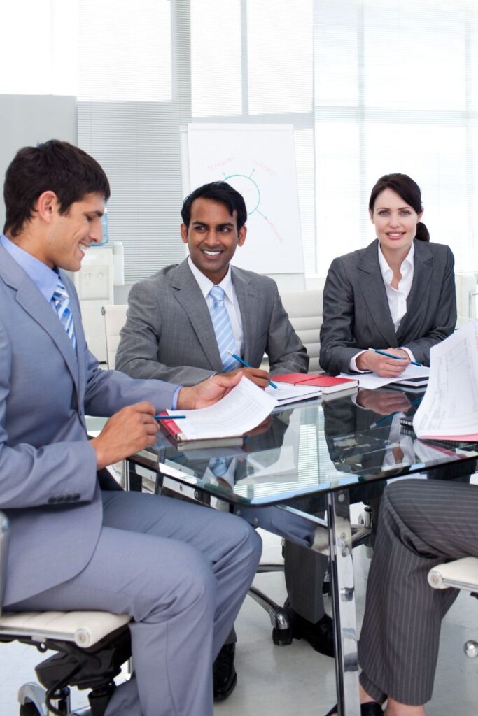 Professionals in a business meeting reviewing documents at a glass table, representing collaboration in an executive search firm.