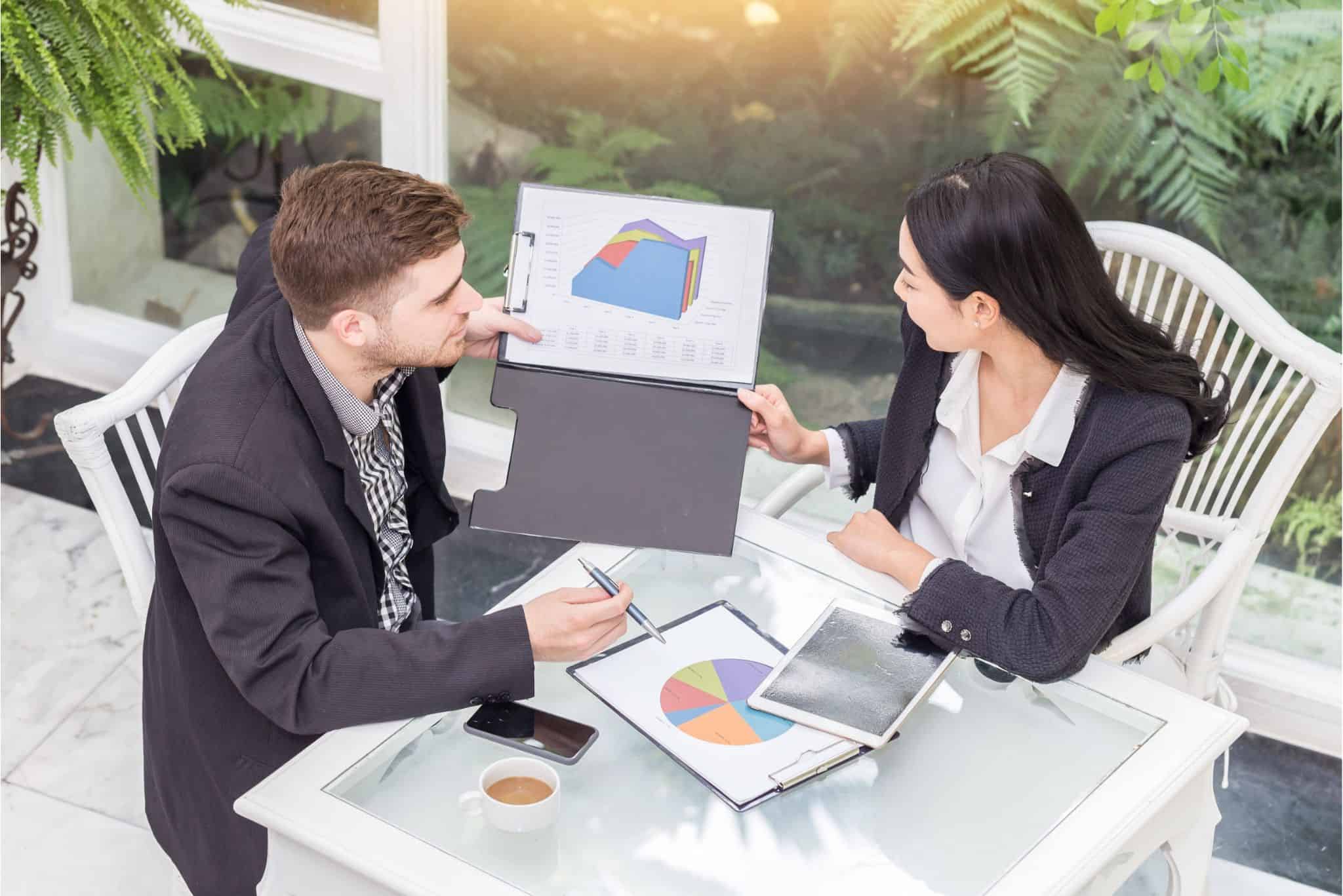 Two professionals in suits reviewing financial charts and pie graphs during an executive search meeting, with a tablet and coffee on the table.