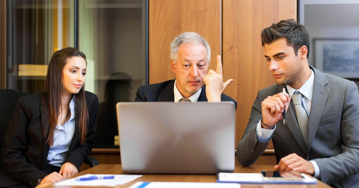 Three focused Education Executive Search Consultants using a laptop and reviewing a strategic plan in an office.