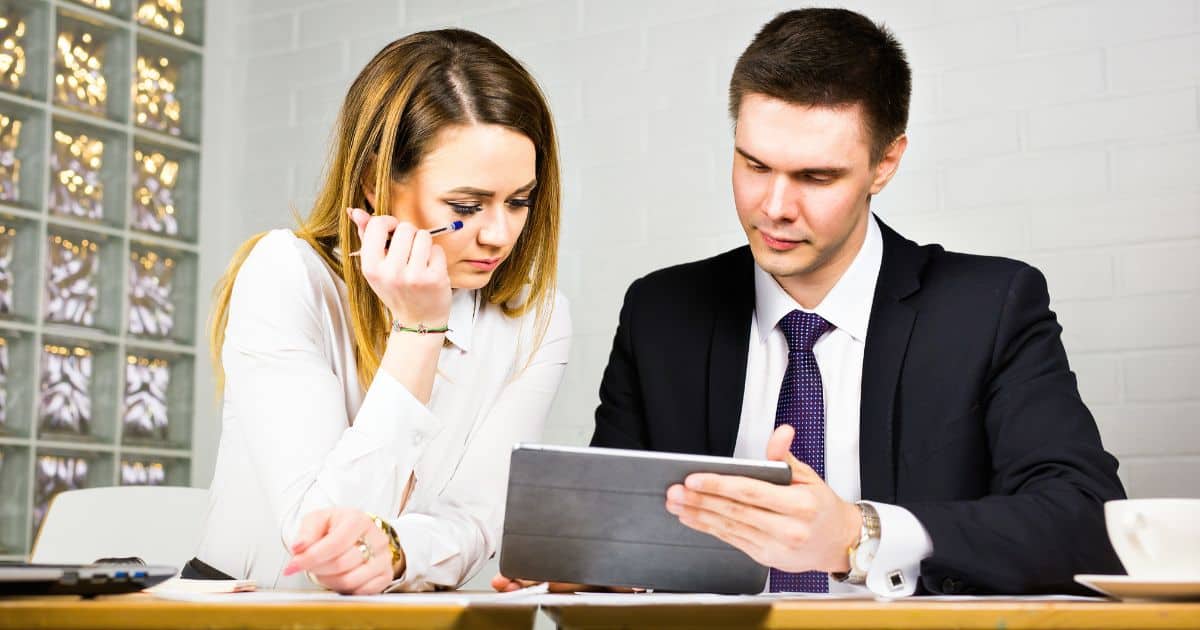 A male and female Retail Executive Search Consultant look intently at a tablet during a meeting.