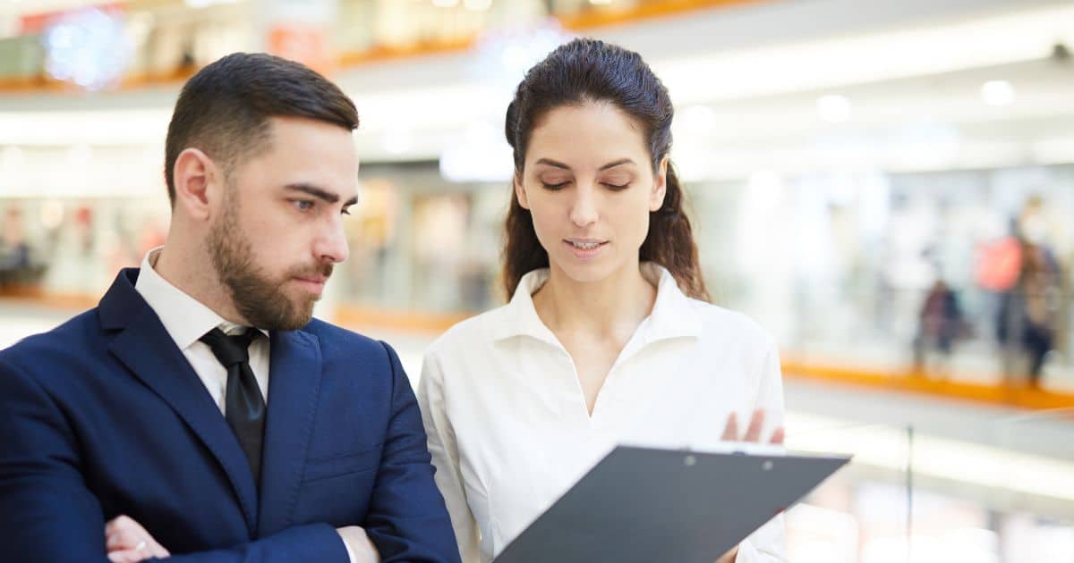 Two professional Retail Executive Search Consultants reviewing documents in a busy mall or retail space.