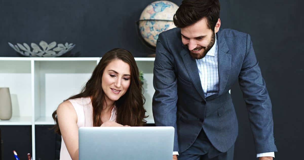 A male and female E-commerce Executive Search Consultant smiling while looking at a laptop screen.