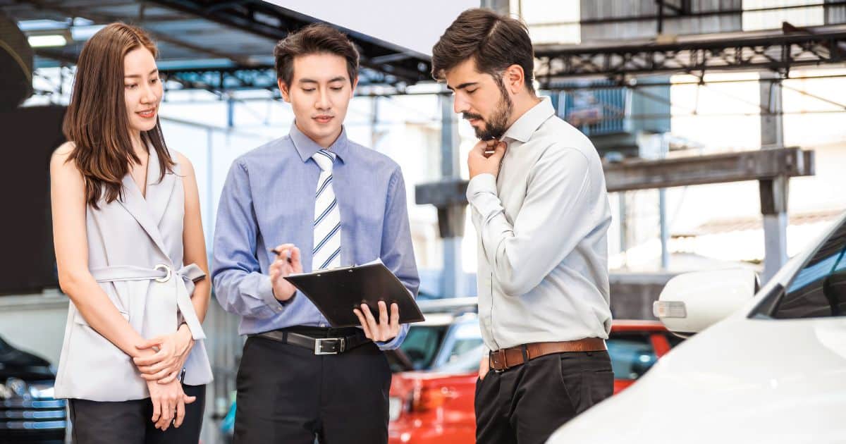 Three professionals—likely Automobile and Auto Executive Search Consultants—meeting in an auto showroom.