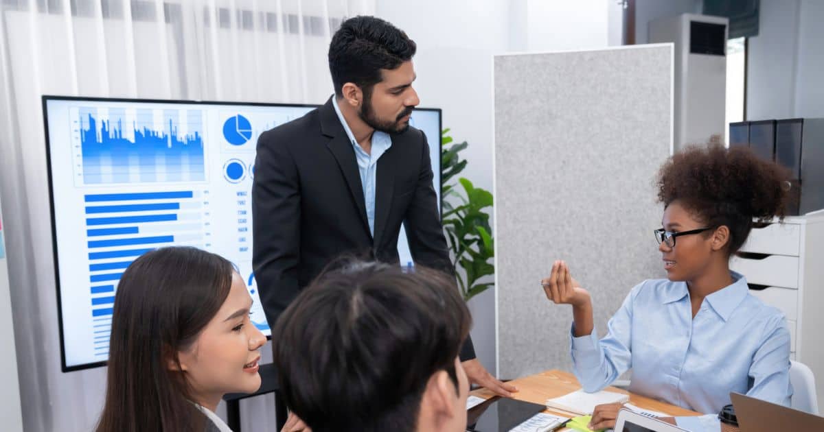 Recruiters in a business meeting discussing hiring strategies with graphs and data on display screen