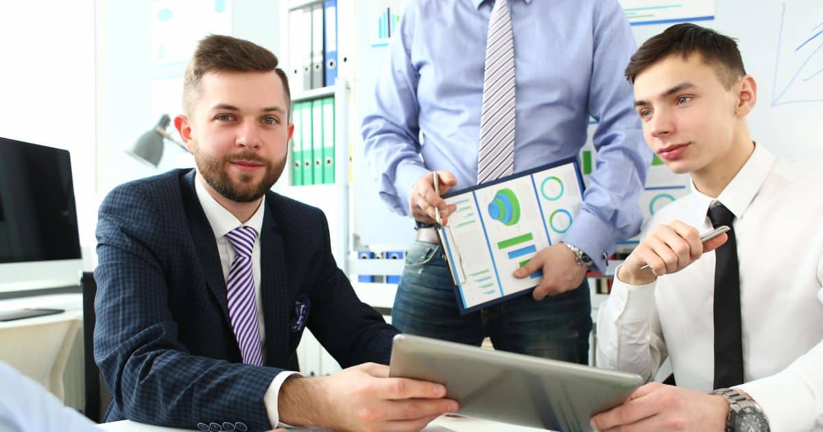 Three professionals working with charts and tablets, highlighting teamwork in executive search efforts.