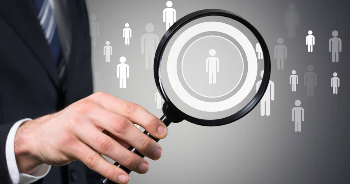 A suited hand holding a magnifier over person icons, depicting professional executive search in a business context.