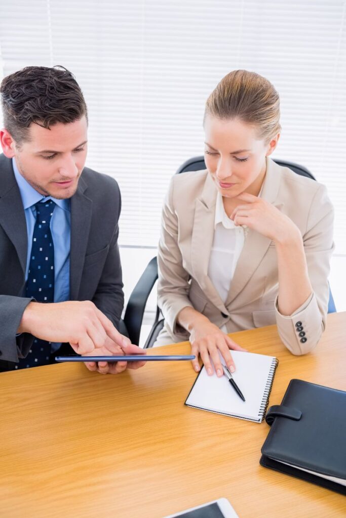 Businessman and businesswoman discussing data on a tablet at an executive search firm meeting.