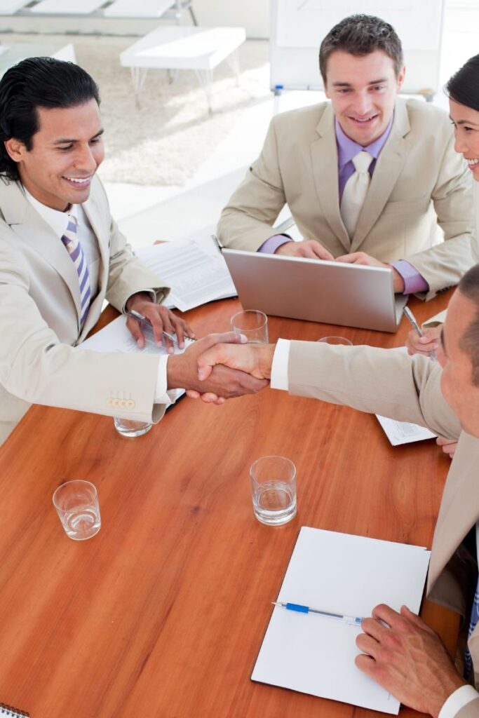 Business professionals shaking hands at a meeting table, symbolizing a successful placement by an executive search firm.
