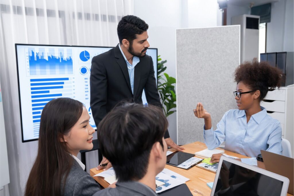 Recruiters in a business meeting discussing hiring strategies with graphs and data on display screen