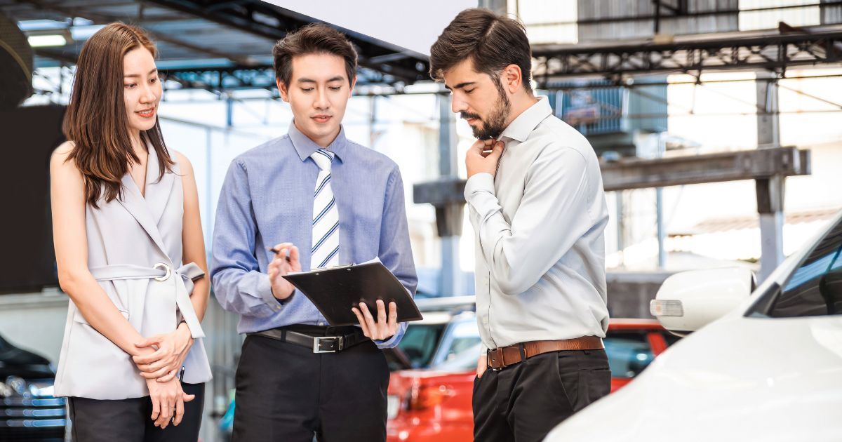 Three professionals—likely Automobile and Auto Executive Search Consultants—meeting in an auto showroom.
