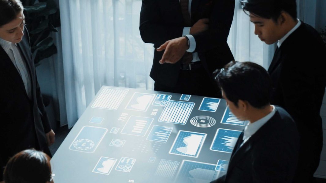 Technology Executive Search: Team Strategy Session business professionals collaborating over a holographic table with data visuals for Technology Executive Search.